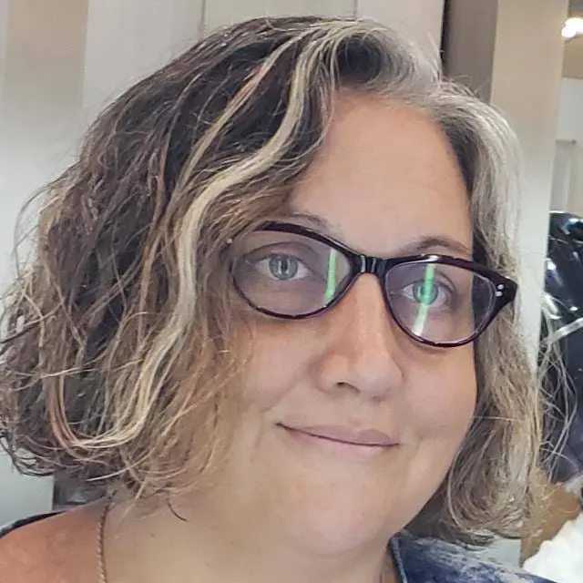 Primer plano de una persona adulta con anteojos y cabello corto ondulado con mechón claro; retrato en interior con fondo desenfocado, imagen de apoyo para nota sobre Orgullo Latinoamérica (OLA).