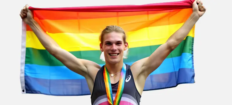 Persona sosteniendo una bandera arcoíris, fondo con colores en explosión”