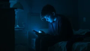 Adolescente sentado en una habitación oscura mira su celular iluminado por una luz azul, en una nota sobre apuestas online, prevención y riesgos para niños, niñas y adolescentes.