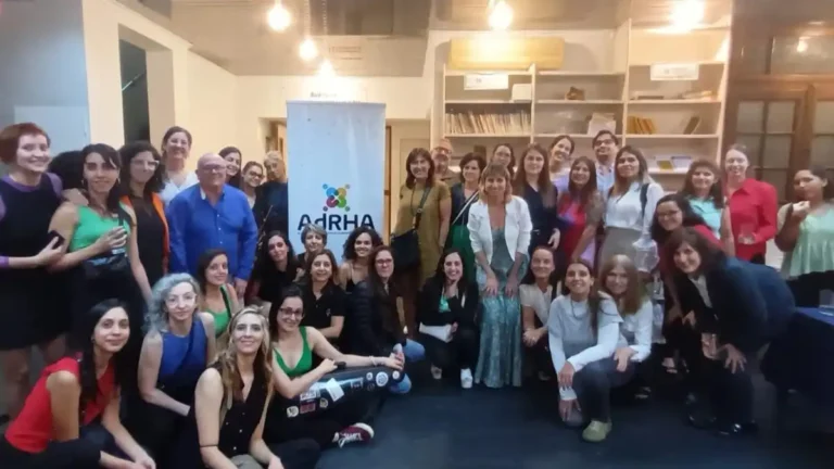 Participantes de la cohorte 2024 de la Certificación DEIB de ADRHA posan en grupo dentro de un salón. En el centro aparece un banner con el nombre y el logotipo de la asociación; algunas personas están de pie y otras, sentadas o arrodilladas.
