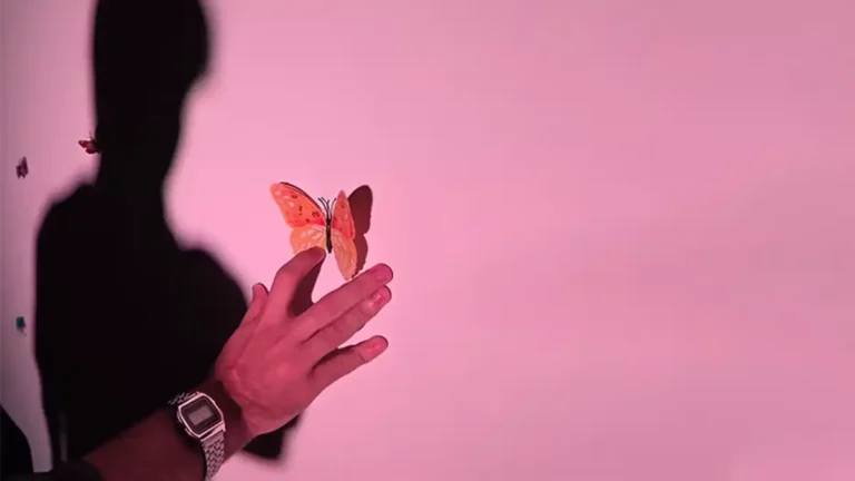 Mano sostiene una mariposa de papel frente a una sombra sobre fondo rosado, en una nota sobre Las nenas también son mariposas, obra teatral que aborda salud mental, adolescencias, duelo y vínculos familiares.