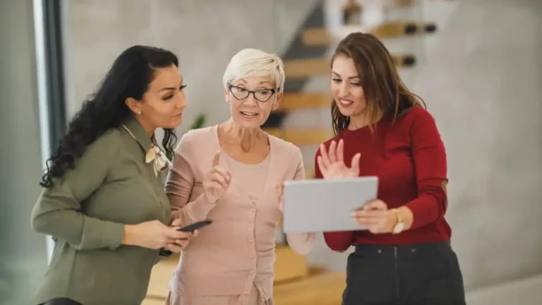 Tres mujeres profesionales conversan mientras revisan una tablet, en una nota sobre redes de mujeres en Argentina para conectar, aprender, fortalecer liderazgos y generar oportunidades.