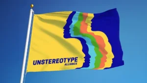 Bandera amarilla de Unstereotype Alliance con perfiles superpuestos de distintos colores y el nombre de la iniciativa sobre un cielo azul.