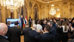 Asistentes reunidos en un salón de estilo clásico frente a un atril, banderas y una pantalla de GNETWORK360.