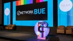 Escenario de GNetwork BUE 360 con pantallas azules y franjas de colores, con sillones a ambos lados.