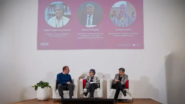 Tres personas participan de un panel frente a una pantalla con la presentación de MIRA sobre mamografía, información, red y acceso.