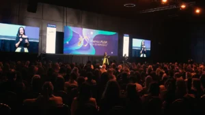 Auditorio lleno durante los Premios FLOR a la Diversidad 2025. En el escenario, una mujer habla frente a una pantalla central con el logo del reconocimiento, mientras otra realiza interpretación en lengua de señas; dos pantallas laterales muestran a la oradora.