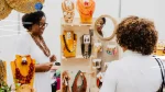 Dos mujeres conversan frente a un puesto con collares, aros y otros accesorios exhibidos.