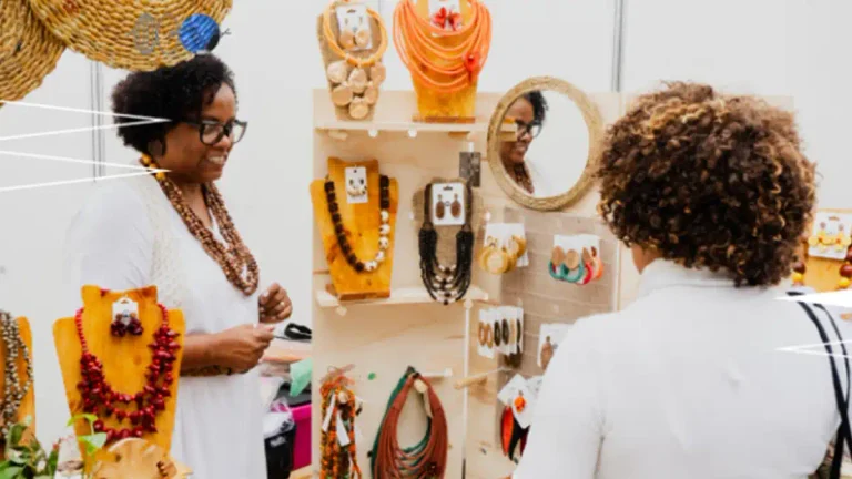 Dos mujeres conversan frente a un puesto con collares, aros y otros accesorios exhibidos.