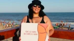Mujer sonriente con sombrero y anteojos en una playa, sosteniendo un cartel que dice “Todos los cuerpos son cuerpos de verano”.