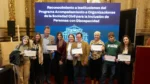 Grupo de representantes de organizaciones posa con certificados frente a la pantalla del Programa de Acompañamiento para la Inclusión de Personas con Discapacidad.