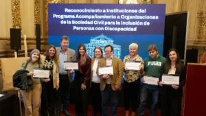 Grupo de representantes de organizaciones posa con certificados frente a la pantalla del Programa de Acompañamiento para la Inclusión de Personas con Discapacidad.