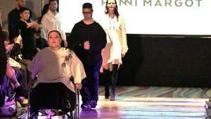 Modelo usuaria de silla de ruedas avanza por una pasarela, seguida por otros dos modelos, con el nombre Panni Margot proyectado al fondo.