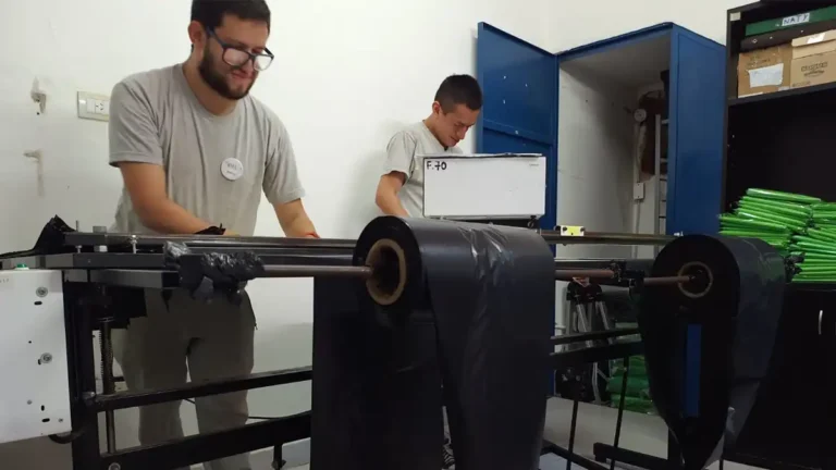 Dos personas trabajan junto a una máquina con rollos de material negro en el taller de Fundación IDEL.