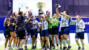 Integrantes de la Selección Argentina femenina de fútbol para ciegas celebran en la cancha mientras levantan el trofeo de campeonas.