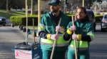 Dos trabajadores de Cliba posan con escobas junto a un carro de limpieza con cartelería de Octubre Rosa, en una acción de concientización sobre el cáncer de mama.