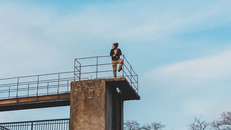 Joven de pie sobre una estructura elevada observa el horizonte bajo un cielo abierto.