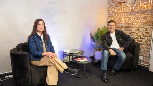 Dos personas sentadas en sillones durante una conversación, con el cartel luminoso “+ allá del diálogo” sobre una pared de ladrillo.